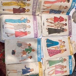 May include: A collection of vintage Simplicity sewing patterns featuring various clothing designs for women. The patterns are printed on white paper with black and red text. The patterns include designs for dresses, pants, skirts, and tops.