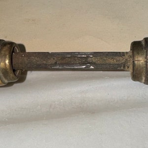 May include: A close-up of a brass door handle with a metal spindle. The handle is worn and has a patina finish.