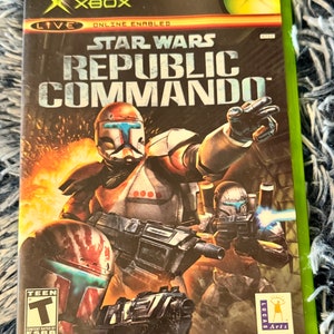 May include: Xbox game case for Star Wars Republic Commando, featuring a green and black background with a red and white armored soldier holding a gun. The game is rated T for Teen by the ESRB.