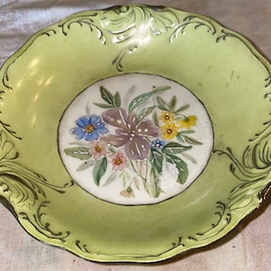 May include: A green and white porcelain dish with a floral design. The dish has a scalloped edge and gold trim.