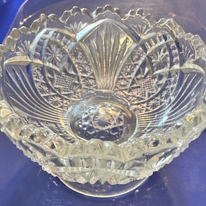 May include: A clear glass bowl with a scalloped edge and intricate cut glass design. The bowl has a footed base and a central design of a flower.
