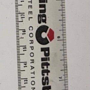 May include: A white plastic ruler with black markings, measuring up to 30 inches. The ruler has the text "Wheeling Pittsburgh STEEL CORPORATION" printed on it.