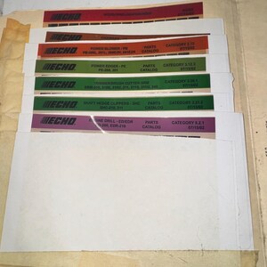 May include: A collection of Echo parts catalogs, featuring various models like chainsaws, power blowers, and trimmers. Each catalog has a colored tab with the Echo logo and model information. The catalogs are organized in a manila folder.