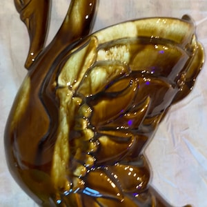 May include: A brown and white ceramic swan planter with a detailed design. The swan's neck is curved and the planter is shaped like a bowl.