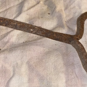 May include: A rusty metal hook with a curved handle. The hook is designed for lifting and moving heavy objects.