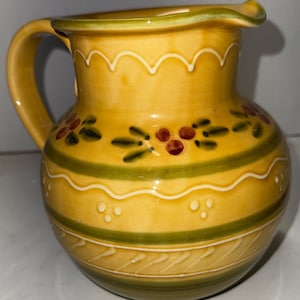 May include: A white ceramic mug with a black handle and the text "But First, Coffee" in a bold, black font. The mug is set against a blurred background, suggesting a cozy setting.