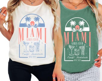 May include: Two tank tops, one cream and one green, with a Miami Girls Club design. The design includes palm trees, beach chairs, cocktails, and the text "Miami Girls Club" and "Emily's Bachelorette AUG 2025".