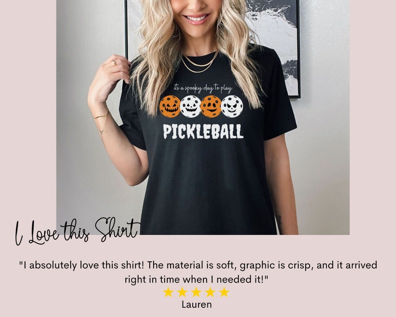 May include: Black t-shirt with a white graphic of three pickleball paddles with jack-o-lantern faces. The text "It's a spooky day to play PICKLEBALL" is on the shirt.