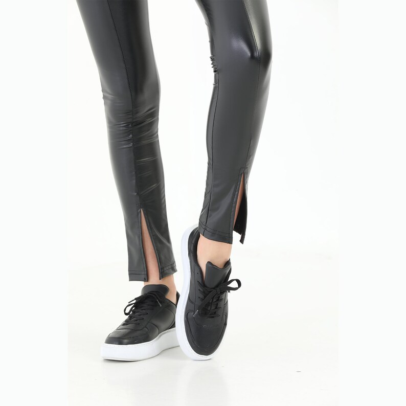 May include: Black faux leather leggings with a slit at the bottom of each leg. The leggings are worn with black sneakers.