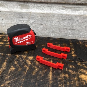 May include: A red and black Milwaukee 25 ft tape measure with three red plastic clips.