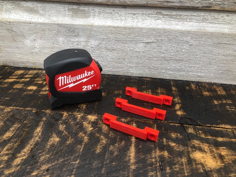 May include: A red and black Milwaukee 25 ft tape measure with three red plastic clips.