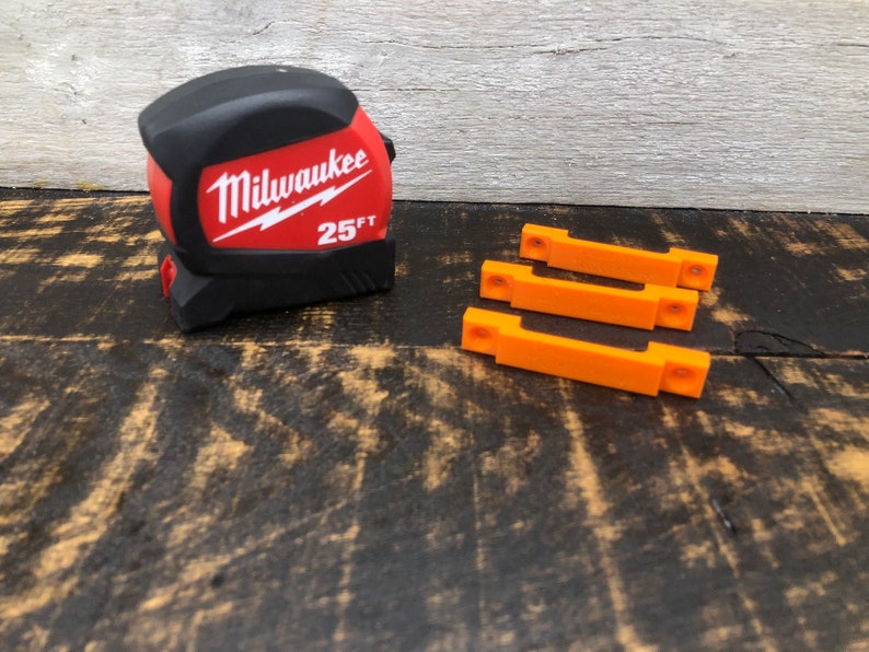 May include: A red and black Milwaukee 25 ft tape measure and three orange plastic wall mounts.