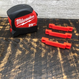 May include: A black and red Milwaukee 25 ft tape measure with three red plastic clips.