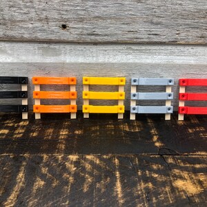 May include: Five small wooden frames with different coloured plastic inserts. The frames are arranged in a row from left to right: black, orange, yellow, grey, and red.