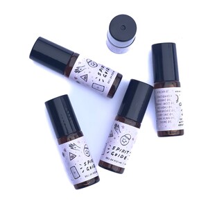 May include: Five brown glass roll-on perfume bottles with black caps. Each bottle has a white label with a pink and purple design and the text "Spirit Guide" and "Roll on Perfume 1 oz".