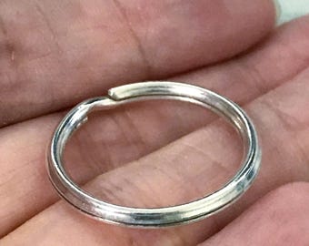 May include: A silver-colored key ring, circular in shape, is held in a person's palm. The key ring is made of a shiny metal and has a simple, elegant design. The key ring is approximately 1 inch in diameter.