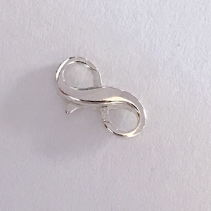 May include: Silver infinity clasp for jewelry making. The clasp is a smooth, shiny metal with a figure eight shape.