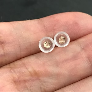 May include: Two clear plastic earring backs with a gold metal post in the center.