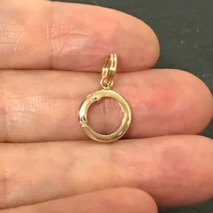 May include: A small, circular gold spring ring clasp featuring a polished metallic finish and a tiny integrated lever mechanism for opening and closing. This jewelry component includes a small attached jump ring at the top for secure attachment.