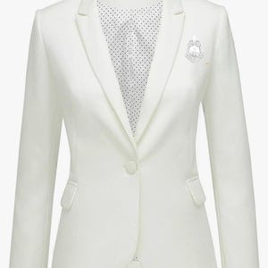 May include: A white blazer with a single-button closure and a notched lapel. The blazer features two front pockets and a decorative pin. The interior lining is white with a black polka dot pattern. This tailored jacket is suitable for formal or business attire.