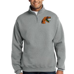 May include: A gray sweatshirt with a zippered neck and a small embroidered snake design on the left chest.