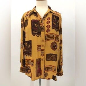 May include: A long-sleeved button-up shirt with a yellow background and a geometric pattern in shades of brown, red, and black. The pattern features stylized animal figures and abstract designs.