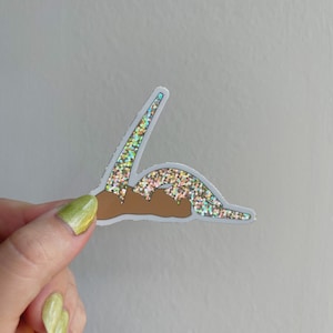 Könnte beinhalten: Ein Aufkleber mit einer Person mit regenbogenfarbenen Glitzerbeinen, die auf dem Bauch liegt. Der Aufkleber befindet sich auf einem weißen Hintergrund.