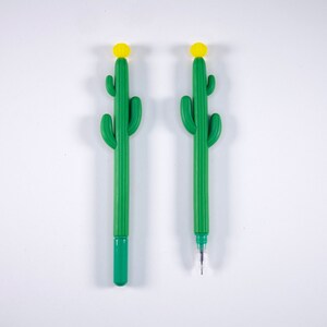 May include: Two green cactus-shaped pens with yellow tops. The pens are on a white background.