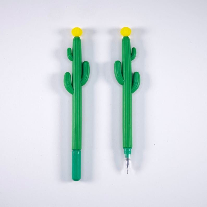 May include: Two green cactus-shaped pens with yellow tops. The pens are on a white background.