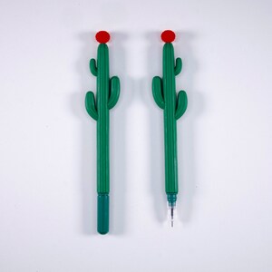 May include: Two green cactus-shaped pens with red flower tops. The pens are on a white background.