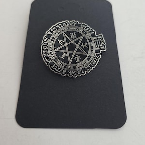 May include: A circular silver-toned metal pin featuring a black enamel inlay with a central pentagram, various symbols, and the text HELLS GATE ARRESTED, HELLSING, GOTT MIT UNS, AND SHINE HEAVEN NOW, along with the number 812 on the right side.