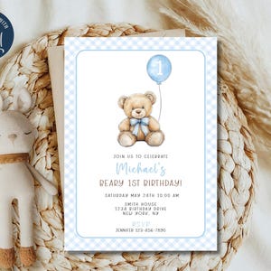 May include: Blue and white checkered invitation with a teddy bear holding a blue balloon with the number 1. The text reads "Join us to celebrate Michael's Beary 1st Birthday! Saturday May 24th 10:00 AM Smith House 1234 Birthday Drive New York, NY RSVP Jennifer 123-456-7890"