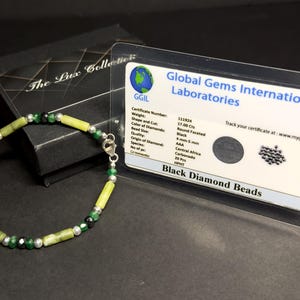 May include: A black diamond bead bracelet with green and yellow stones. The bracelet is accompanied by a certificate from Global Gems International Laboratories, stating the weight, shape, cut, color, quality, species, and origin of the diamonds. The certificate number is 131924.