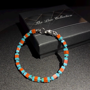 May include: A turquoise and orange beaded bracelet with a silver clasp. The bracelet is on a black box with the text "The Lux Collection".