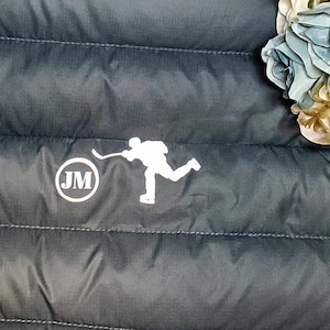 May include: A dark blue puffer jacket with a white hockey player graphic and a white circle with the initials "JM" in the center.