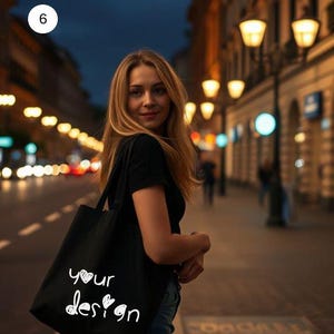 May include: A woman in a black shirt and jeans is carrying a black tote bag with the words "your design" written on it in white.