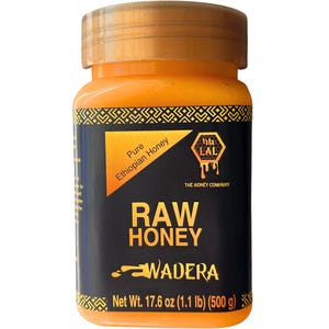 May include: A jar of raw honey with a golden lid and a black label. The label features the text "RAW HONEY" and "WADERA" in white, with "Pure Ethiopian Honey" in a yellow triangle. The jar contains 17.6 oz (1.1 lb) or 500 g of honey.