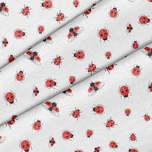 May include: White fabric featuring a repeating pattern of red ladybirds with black spots and outlines. Some ladybirds have open wings, and the design is scattered across the fabric.