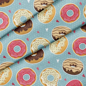 May include: A seamless pattern featuring a variety of donuts with different toppings, including chocolate, sprinkles, and white frosting. The donuts are arranged on a light blue background with white polka dots and pink hearts.