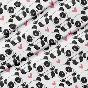 Puede incluir: Tela blanca con un patrón repetido de osos panda blancos y negros y corazones rosas. Los pandas están dibujados en un estilo de dibujos animados con ojos grandes y caras sonrientes.