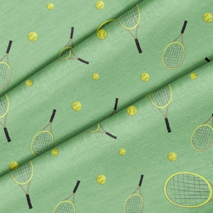 May include: Green fabric with a repeating pattern of tennis rackets and tennis balls. The rackets are yellow and black, and the balls are yellow.