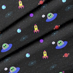 May include: Black fabric with a repeating pattern of spaceships, aliens, planets, and stars. The fabric has a subtle sparkle.