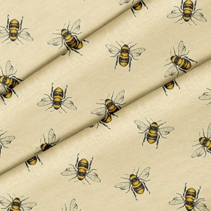 Puede incluir: Una tela beige con un patrón repetido de abejas amarillas y negras. Las abejas están dibujadas en un estilo vintage.