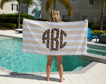May include: A white and beige striped beach towel with a large, round, leopard print monogram "ABC" in the center.