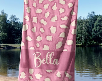 May include: Pink beach towel with a white leopard print and the name "Bella" printed in white on the bottom.