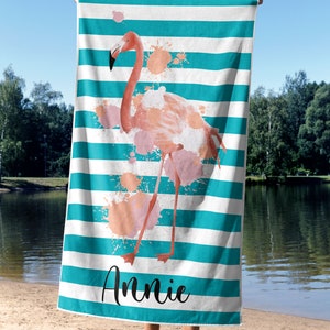 May include: A turquoise and white striped beach towel with a pink flamingo illustration and pink watercolor splatters. The towel has the name "Annie" printed on the bottom.