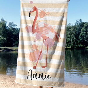 May include: A beach towel with a pink flamingo illustration and watercolor splatters. The towel has white and beige stripes and the name "Annie" is written in black cursive.