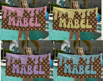 May include: Four beach towels with a waffle cone and ice cream design. The towels are in different colors with the name "MABEL" printed on each towel.
