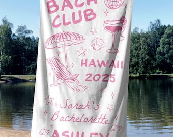 Puede incluir: Toalla de playa blanca con texto e ilustraciones rosas. La toalla dice "THE BACH CLUB HAWAII 2025 Sarah's Bachelorette ASHLEY" con imágenes de un cóctel, bola de discoteca, sombrilla y tumbona.
