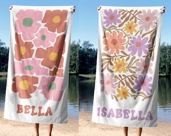 May include: Two white beach towels with floral designs. One features pink and brown flowers with the name "BELLA" in a retro font. The other towel has a design of orange, yellow, and purple flowers with the name "ISABELLA".